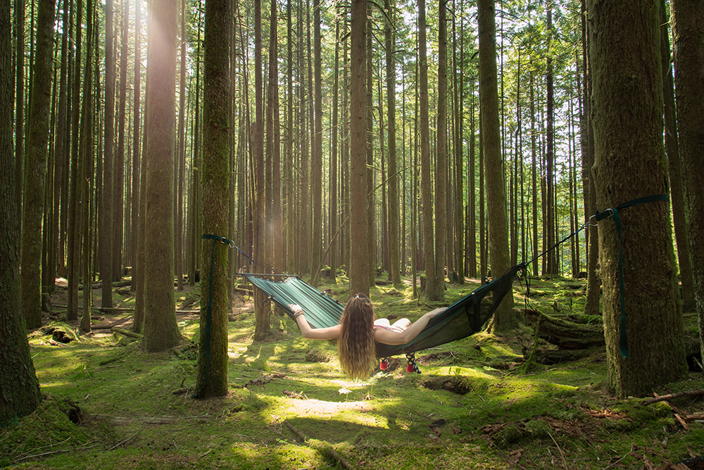 A girl in a Lawson hammock hanging in a lush green forest