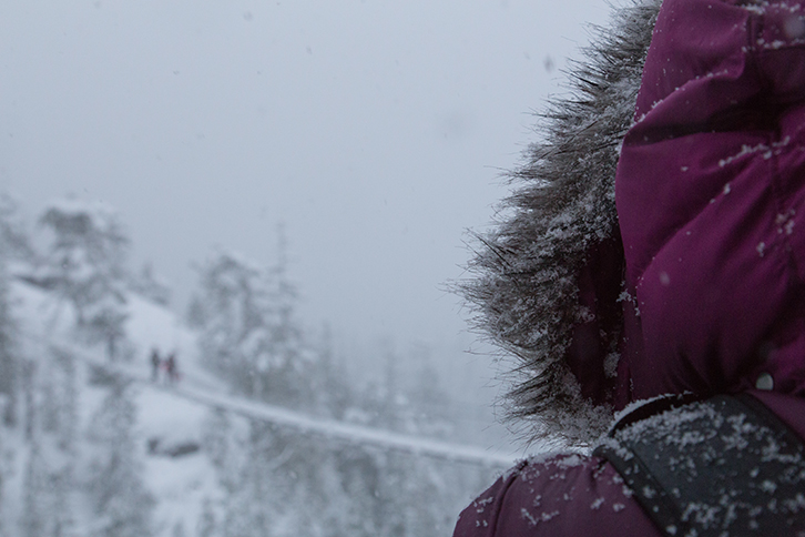 A person with a big fuzzy hood looks out at the snow at the sea to sky gondola